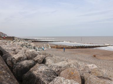 A rocky beachfront with wooden groynes stretching into the sea and a few people and a dog on the beach at The Old Station House in Withernsea