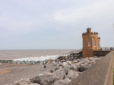 A beach with rocky shoreline and a small castle-like structure near the sea at The Old Station House in Withernsea