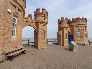 A brick castle-like structure with two towers and benches near a waterfront at The Old Station House in Withernsea