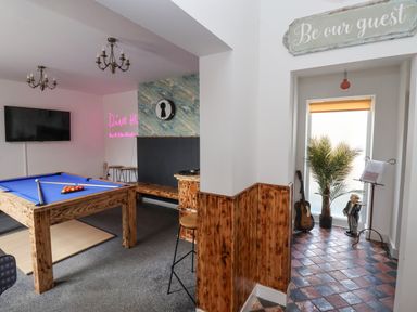 A game room with a pool table a television wooden benches and stools a guitar and a plant near a window at The Old Station House in Withernsea
