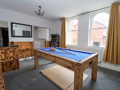 A game room with a pool table, bar stools, an arcade machine, and large windows with curtains at The Old Station House in Withernsea