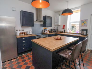 A kitchen with blue cabinets a wooden island two brown chairs and stainless steel appliances at The Old Station House in Withernsea
