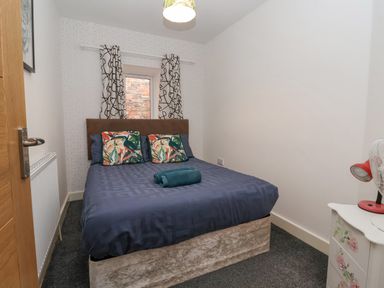 A bedroom with a bed two pillows two towels a window with curtains a radiator and a bedside table with a fan and lamp at The Old Station House in Withernsea