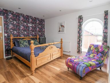 A bedroom with a wooden bed a colorful chaise lounge and floral curtains at The Old Station House in Withernsea