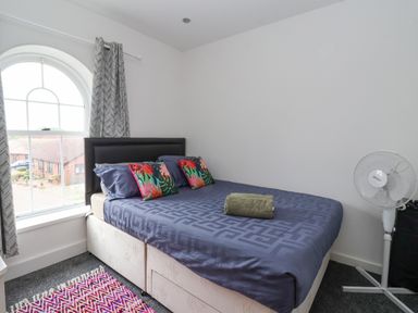 A bedroom with a bed with colorful pillows a rolled towel on the bed a standing fan and a window with curtains at The Old Station House in Withernsea