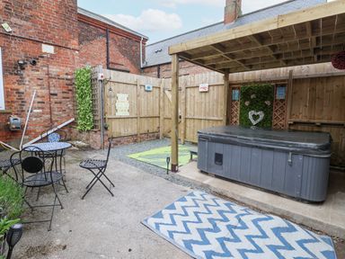 An outdoor patio area with a hot tub under wooden pergola a small table with chairs and rugs on the ground at The Old Station House in Withernsea