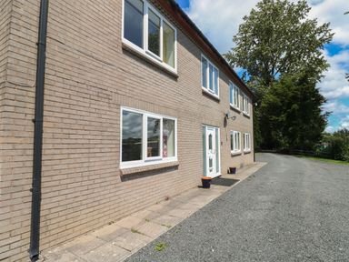 The exterior of a two-story brick house with several windows a white front door and a gravel driveway with trees in the background at Hillside Lodge in Newtown