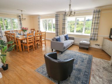 A living and dining area with wooden dining table and chairs and grey sofa with windows showing countryside views at Hillside Lodge in Newtown