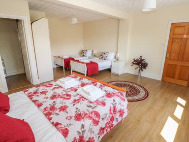 A bedroom with three beds two single beds and one double bed with red floral bedding and wooden floor at Hillside Lodge in Newtown