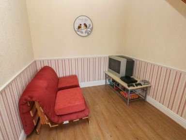 A small room with a red foldable sofa a television on a low table and a round wall clock at Hillside Lodge in Newtown