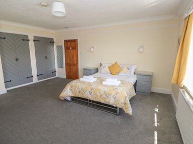 A bedroom with a double bed with floral bedding and pillows two bedside tables a wooden door built in wardrobes with grey doors a window with yellow curtains and grey carpet at Hillside Lodge in Newtown