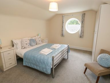 A bedroom with a double bed with blue bedding and pillows bedside tables a round window curtains a chair with a blue cushion and a wardrobe at Hillside Lodge in Newtown