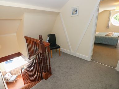A hallway with carpeted floor, wooden stair railing, a black chair, and a view into a bedroom with a bed at Hillside Lodge in Newtown