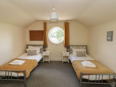 A bedroom with two single beds with bedside tables and lamps and a round window at Hillside Lodge in Newtown