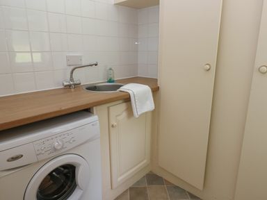 A laundry room with a washing machine wooden countertop a sink and cabinets at Hillside Lodge in Newtown