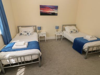 A bedroom with two single beds blue throws and bedside tables with lamps at Hillside Lodge in Newtown
