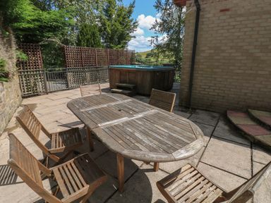 An outdoor patio area with a wooden table and six chairs and a hot tub in the background at Hillside Lodge in Newtown