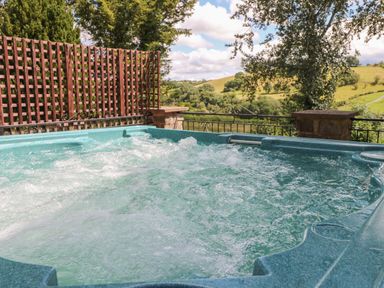 An outdoor hot tub with bubbling water and a view of green hills and trees at Hillside Lodge in Newtown