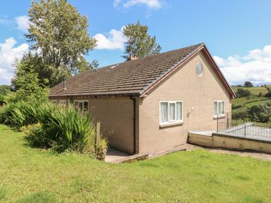 A brick house with a pitched roof and windows surrounded by grass and trees at Hillside Lodge in Newtown