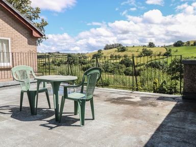 A rooftop patio with two green plastic chairs and a table overlooking green hills and trees at Hillside Lodge in Newtown