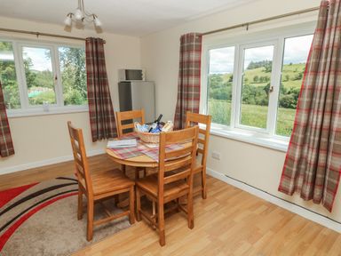 A dining area with a round wooden table and four chairs next to large windows with plaid curtains and a small fridge with a microwave on top at Hillside Lodge in Newtown