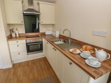 A kitchen with wooden countertops a stainless steel oven and sink with tea cups cake and a teapot on the counter at Hillside Lodge in Newtown