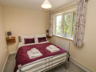 A bedroom with a double bed with two folded towels purple bedding two bedside shelves and a window with curtains at Hillside Lodge in Newtown
