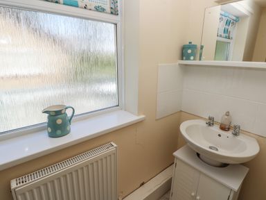 A bathroom with a white sink cabinet a faucet a blue polka dot jug on the window sill and a blue polka dot container on the shelf at Hillside Lodge in Newtown