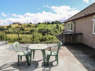 A patio with a round table and two chairs overlooking green hills at Hillside Lodge in Newtown