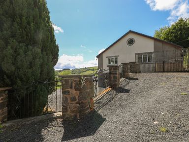 A gravel driveway with stone pillars and metal gate leading to a house with a circular window at Hillside Lodge in Newtown