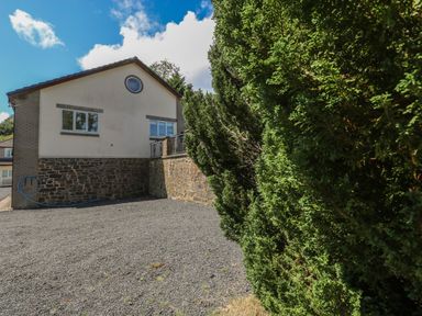 A house with stone and brick walls next to a gravel area and tall green bushes at Hillside Lodge in Newtown