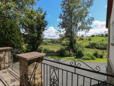 A metal gate and stone pillars with a gravel driveway and green hills in the background at Hillside Lodge in Newtown