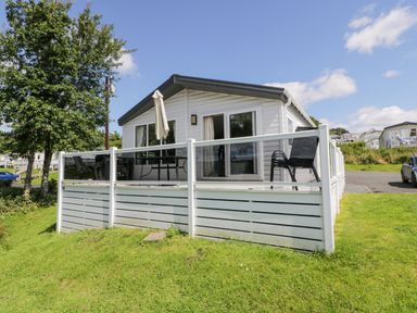 A white mobile home with a glass railing deck and outdoor furniture on grass at Olivias Haven in Wemyss Bay