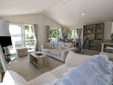 A living room with sofas coffee table tv dining table and chairs with windows showing outdoor view at Olivias Haven in Wemyss Bay