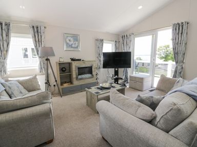 A living room with two sofas a coffee table a TV a fireplace and windows at Olivias Haven in Wemyss Bay