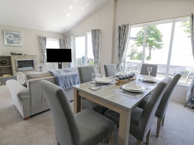 A dining area with a table set for six next to a living room with a sofa and television at Olivia's Haven in Wemyss Bay
