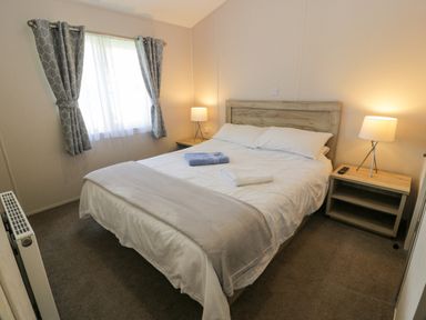 A bedroom with a double bed two bedside tables with lamps and a window with curtains at Olivias Haven in Wemyss Bay