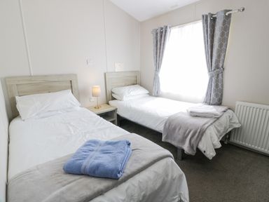 A bedroom with two single beds a bedside table with a lamp and a window with curtains at Olivias Haven in Wemyss Bay