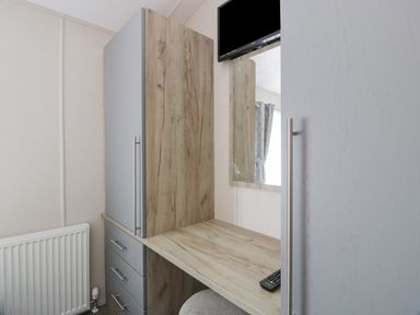A wooden desk with a built-in wardrobe and drawers next to a radiator and a wall mirror with a TV mounted above at Olivias Haven in Wemyss Bay
