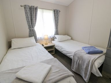 A bedroom with two single beds a nightstand a lamp and folded towels at Olivias Haven in Wemyss Bay