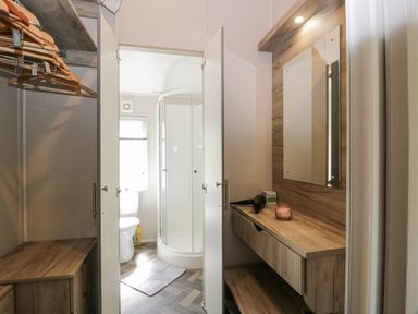A bathroom with a shower and toilet visible through double doors and a wooden vanity with a mirror and hangers in a closet at Olivias Haven in Wemyss Bay