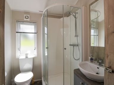 A bathroom with a toilet under a window a glass shower enclosure and a sink with a mirror at Olivias Haven in Wemyss Bay