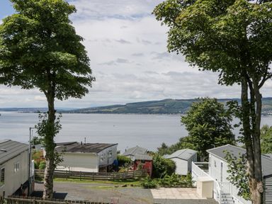 A view of a lake with trees and buildings in the foreground at Olivias Haven in Wemyss Bay