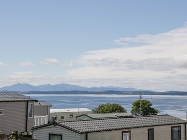 Rooftops of mobile homes with a body of water and mountains in the background at Olivias Haven in Wemyss Bay