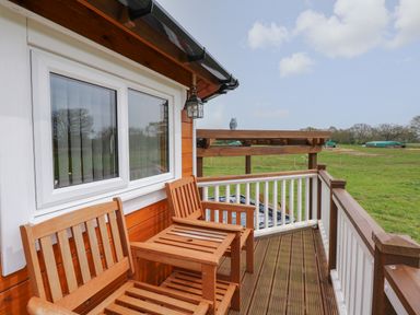 A wooden balcony with two wooden chairs and a table overlooking a green field at Dragonfly Retreat in Upper Marham