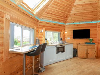 A kitchen area with bar stools countertop microwave and wall mounted television at Dragonfly Retreat in Upper Marham