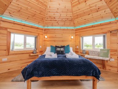 A wooden bedroom with a double bed with blue bedding and pillows between two windows at Dragonfly Retreat in Upper Marham