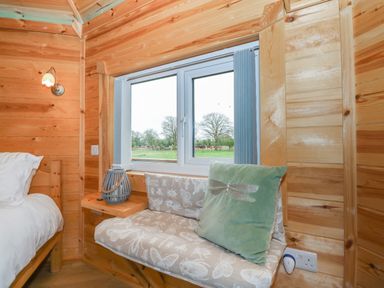 A wooden room corner with a white bed pillow wall lamp window seat with patterned cushion and green pillow at Dragonfly Retreat in Upper Marham