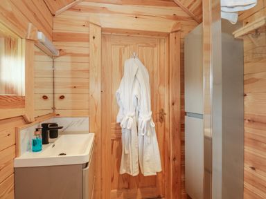 A bathroom with a wooden door and white robes hanging on it and a sink with a black faucet and a mirror at Dragonfly Retreat in Upper Marham