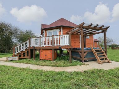 A wooden cabin with a deck and stairs leading to grass at Dragonfly Retreat in Upper Marham